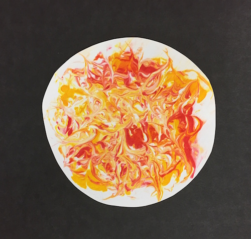 the cut out sun shape with swirls of food coloring mounted on a black piece of paper